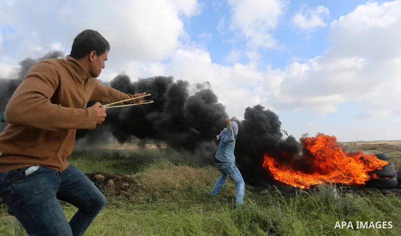 Palestinian protesters use slingshot to hurl stones towards Isareli security forces during clashes in a tent city protest at along the Israel border with Gaza, demanding the right to return to their homeland, in al-Burei...
