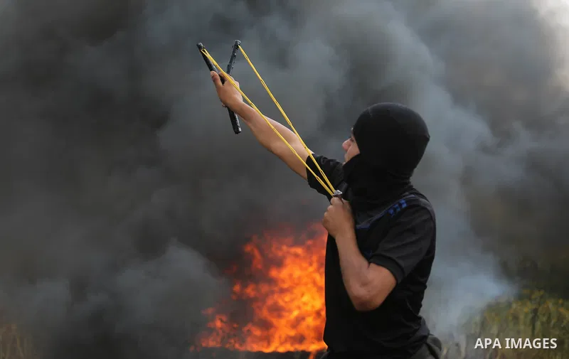 A Palestinian protester uses a slingshot to hurl stones towards Israeli security forces during clashes in a tent city protest along the Israel border with Gaza, demanding the right to return to their homeland, in Khan Yo...