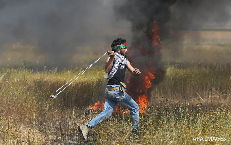 A Palestinian protester uses a slingshot to hurl stones towards Israeli security forces during clashes in a tent city protest along the Israel border with Gaza, demanding the right to return to their homeland, in Khan Yo...