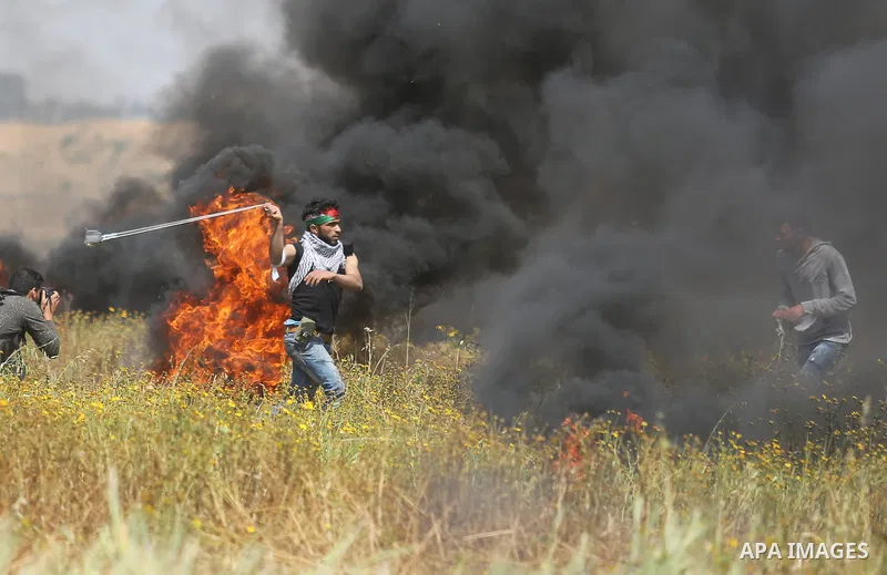 A Palestinian protester uses a slingshot to hurl stones towards Israeli security forces during clashes in a tent city protest along the Israel border with Gaza, demanding the right to return to their homeland, in Khan Yo...