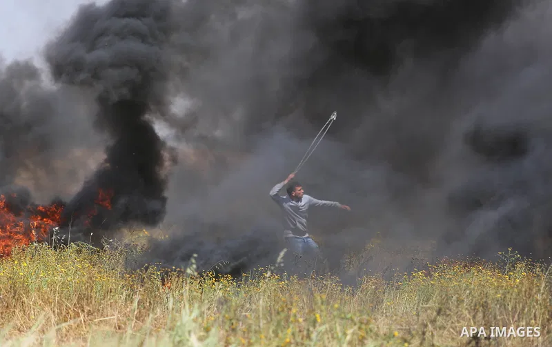 A Palestinian protester uses a slingshot to hurl stones towards Israeli security forces during clashes in a tent city protest along the Israel border with Gaza, demanding the right to return to their homeland, in Khan Yo...