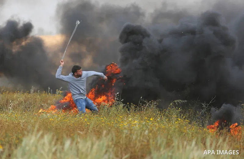 A Palestinian protester uses a slingshot to hurl stones towards Israeli security forces during clashes in a tent city protest along the Israel border with Gaza, demanding the right to return to their homeland, in Khan Yo...