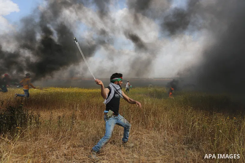 A Palestinian protester uses a slingshot to hurl stones towards Israeli security forces during clashes in a tent city protest along the Israel border with Gaza, demanding the right to return to their homeland, in Khan Yo...