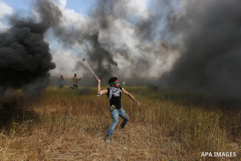 A Palestinian protester uses a slingshot to hurl stones towards Israeli security forces during clashes in a tent city protest along the Israel border with Gaza, demanding the right to return to their homeland, in Khan Yo...