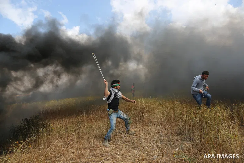 A Palestinian protester uses a slingshot to hurl stones towards Israeli security forces during clashes in a tent city protest along the Israel border with Gaza, demanding the right to return to their homeland, in Khan Yo...