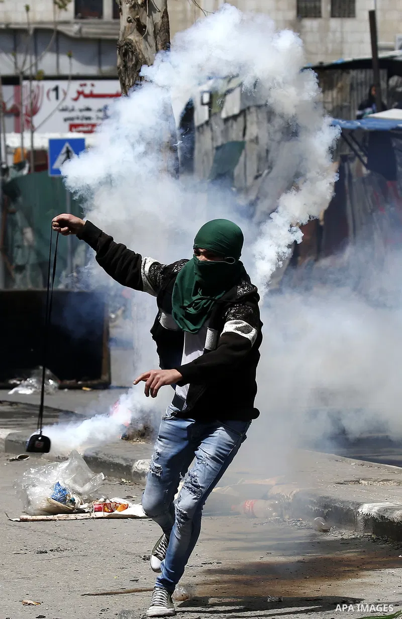 A Palestinian protester uses a slingshot to throw back a tear gas canister fired by Israeli security forces during clashes on March 31, 2018 in occupied West Bank city of Hebron as a general strike is called for by local...