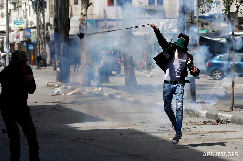 A Palestinian protester uses a slingshot to hurl stones towards Israeli security forces during clashes on March 31, 2018 in occupied West Bank city of Hebron as a general strike is called for by local leaders in solidari...