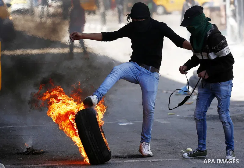 A Palestinian protester kicks a burning tire towards Israeli security forces during clashes on March 31, 2018 in occupied West Bank city of Hebron as a general strike is called for by local leaders in solidarity with Gaz...
