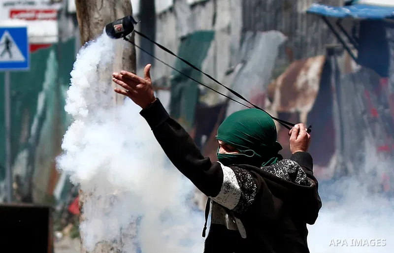 A Palestinian protester uses a slingshot to throw back a tear gas canister fired by Israeli security forces during clashes on March 31, 2018 in occupied West Bank city of Hebron as a general strike is called for by local...