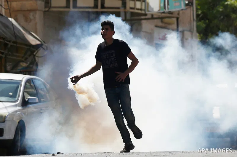 A Palestinian protester throws back a tear gas canister fired by Israeli security forces during clashes on March 31, 2018 in occupied West Bank city of Hebron as a general strike is called for by local leaders in solidar...