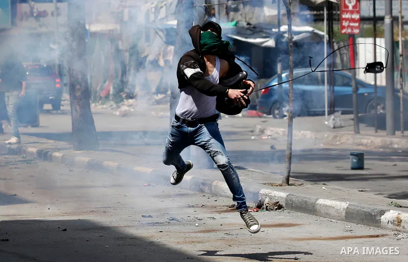 A Palestinian protester uses a slingshot to hurl stones towards Israeli security forces during clashes on March 31, 2018 in occupied West Bank city of Hebron as a general strike is called for by local leaders in solidari...