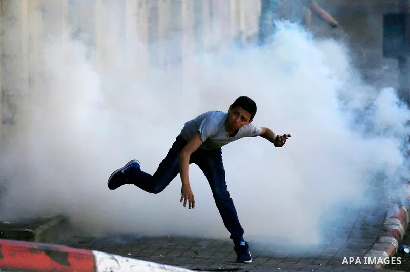 A Palestinian protester throws back a tear gas canister fired by Israeli security forces during clashes on March 31, 2018 in occupied West Bank city of Hebron as a general strike is called for by local leaders in solidar...