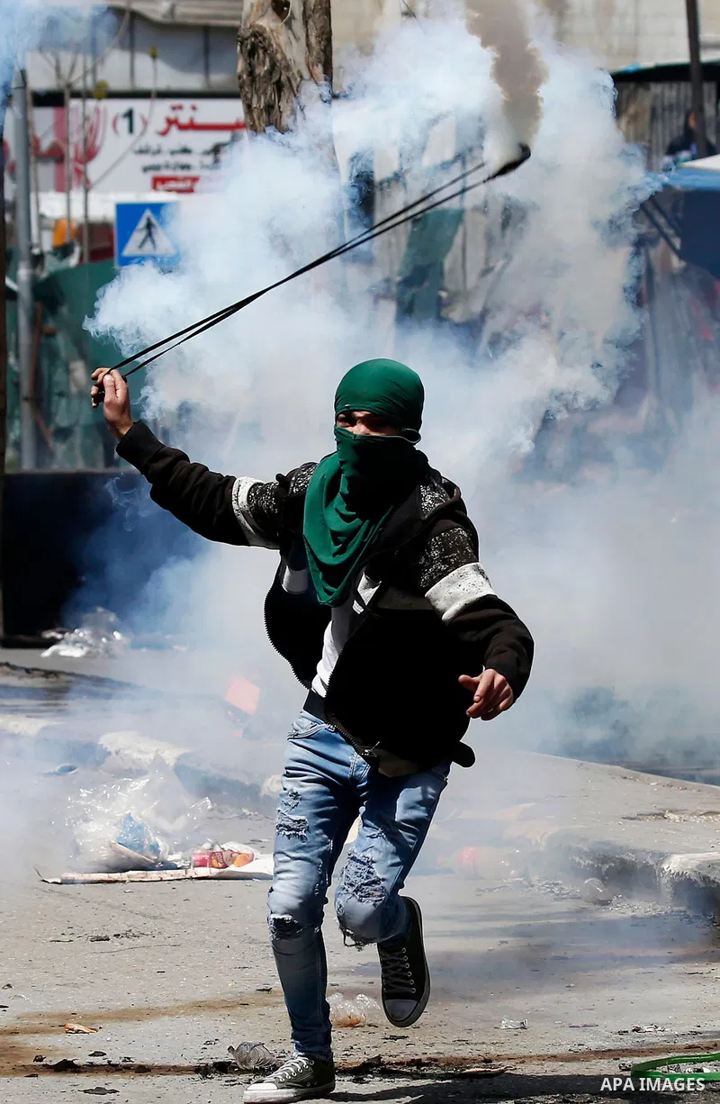 A Palestinian protester uses a slingshot to throw back a tear gas canister fired by Israeli security forces during clashes on March 31, 2018 in occupied West Bank city of Hebron as a general strike is called for by local...