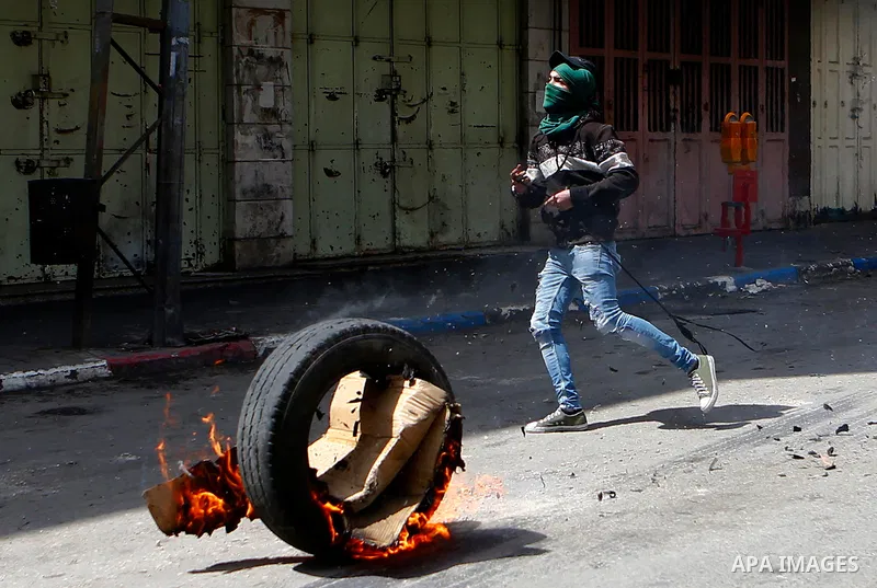 A Palestinian protester uses a slingshot to hurl stones towards Israeli security forces during clashes on March 31, 2018 in occupied West Bank city of Hebron as a general strike is called for by local leaders in solidari...
