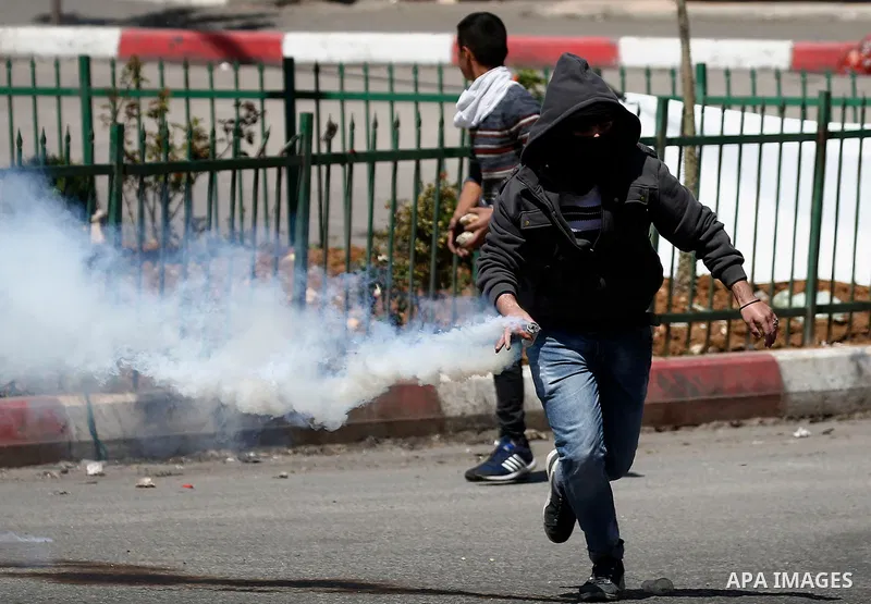 A Palestinian protester throws back a tear gas canister fired by Israeli security forces during clashes on March 31, 2018 in occupied West Bank city of Hebron as a general strike is called for by local leaders in solidar...