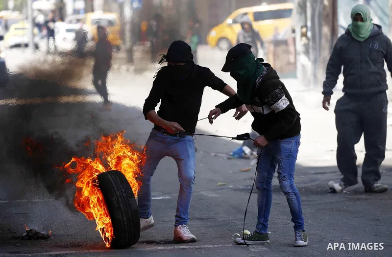 A Palestinian protester kicks a burning tire towards Israeli security forces during clashes on March 31, 2018 in occupied West Bank city of Hebron as a general strike is called for by local leaders in solidarity with Gaz...
