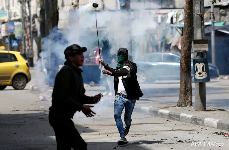 A Palestinian protester uses a slingshot to throw back a tear gas canister fired by Israeli security forces during clashes on March 31, 2018 in occupied West Bank city of Hebron as a general strike is called for by local...