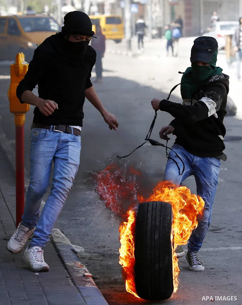 A Palestinian protester kicks a burning tire towards Israeli security forces during clashes on March 31, 2018 in occupied West Bank city of Hebron as a general strike is called for by local leaders in solidarity with Gaz...