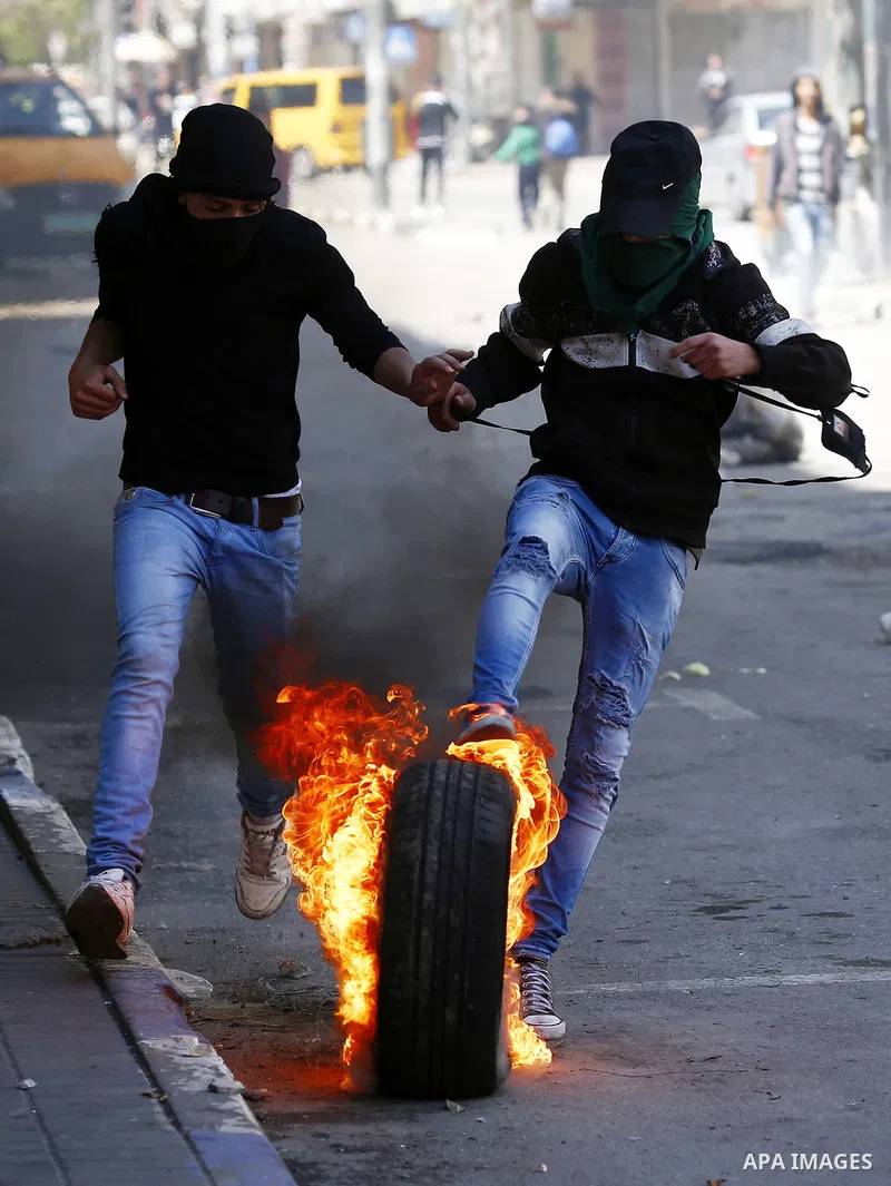A Palestinian protester kicks a burning tire towards Israeli security forces during clashes on March 31, 2018 in occupied West Bank city of Hebron as a general strike is called for by local leaders in solidarity with Gaz...