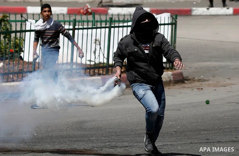 A Palestinian protester throws back a tear gas canister fired by Israeli security forces during clashes on March 31, 2018 in occupied West Bank city of Hebron as a general strike is called for by local leaders in solidar...