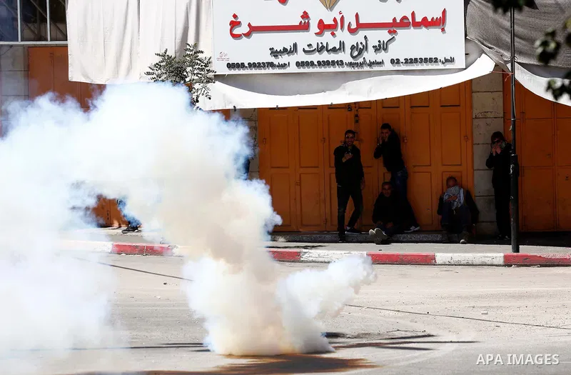 Palestinian protesters take cover form a tear gas canister fired by Israeli security forces during clashes on March 31, 2018 in occupied West Bank city of Hebron as a general strike is called for by local leaders in soli...