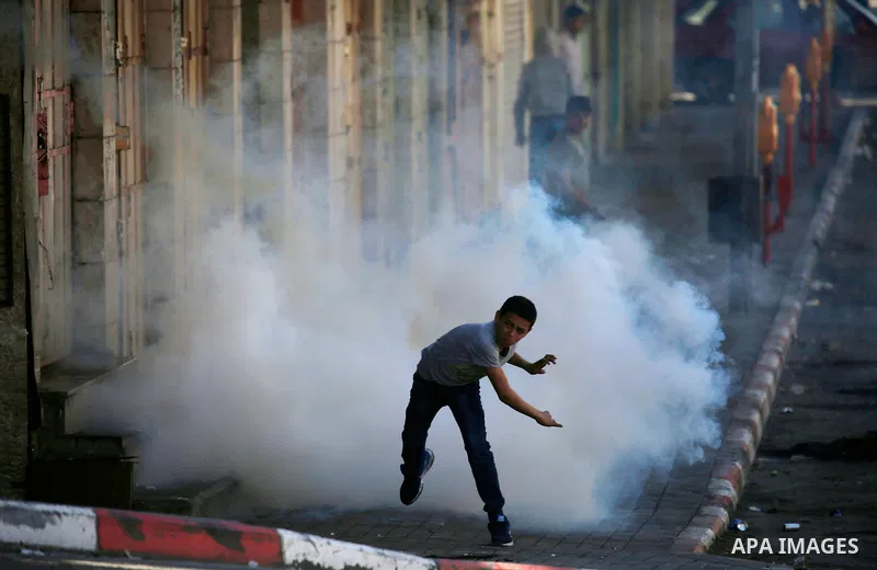 A Palestinian protester throws back a tear gas canister fired by Israeli security forces during clashes on March 31, 2018 in occupied West Bank city of Hebron as a general strike is called for by local leaders in solidar...