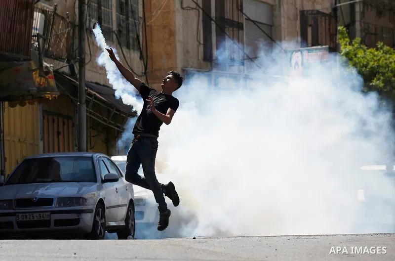 A Palestinian protester throws back a tear gas canister fired by Israeli security forces during clashes on March 31, 2018 in occupied West Bank city of Hebron as a general strike is called for by local leaders in solidar...