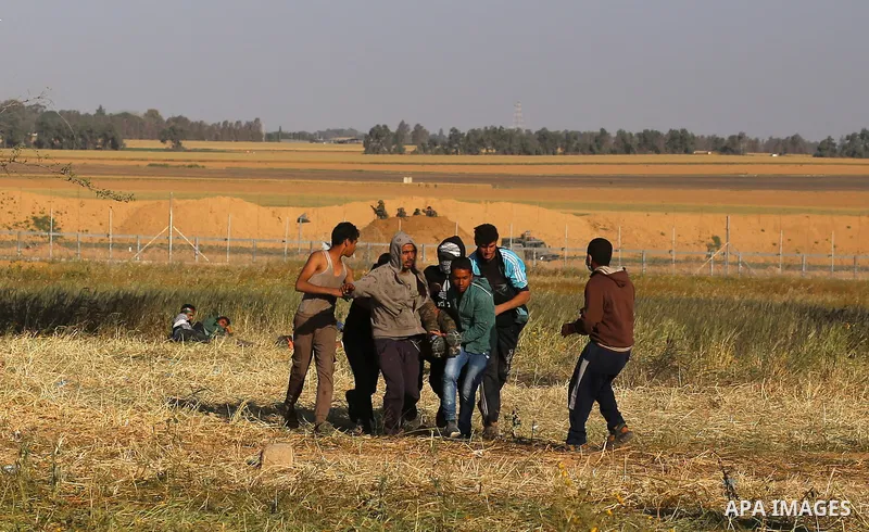An injured Palestinian man is carried by protesters as they run for cover during a protest along the border with Israel, east of Khan Yunis, in the southern Gaza Strip on March 31, 2018. The UN Security Council heard fea...