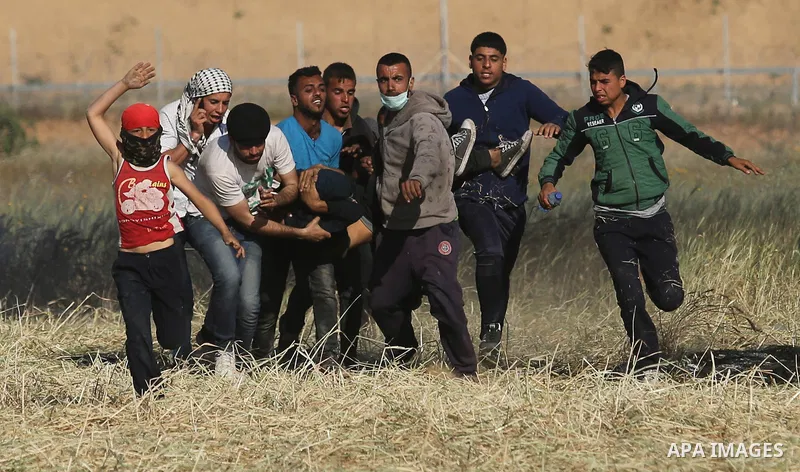 An injured Palestinian man is carried by protesters as they run for cover during a protest along the border with Israel, east of Khan Yunis, in the southern Gaza Strip on March 31, 2018. The UN Security Council heard fea...