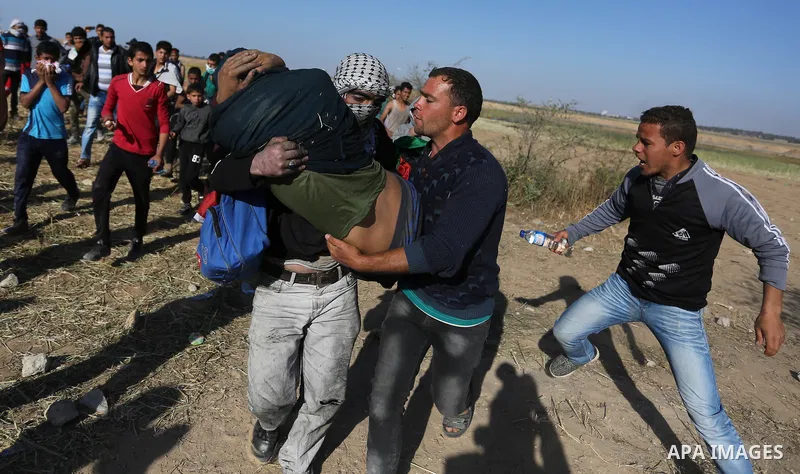 An injured Palestinian man is carried by protesters as they run for cover during a protest along the border with Israel, east of Khan Yunis, in the southern Gaza Strip on March 31, 2018. The UN Security Council heard fea...