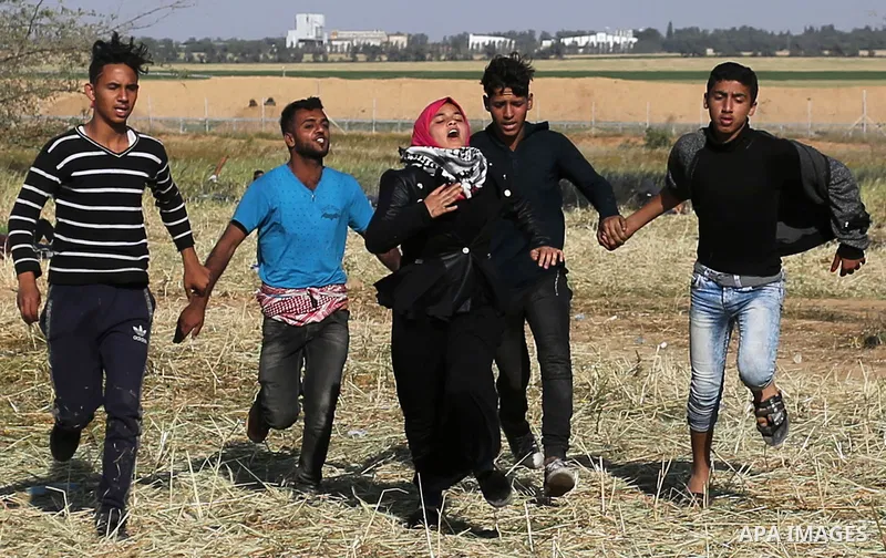 Palestinian protesters hold hands to protect a girl from shots as they run for cover during clashes with Israeli security forces following a demonstration near the border with Israel, east of Khan Yunis, in the southern...