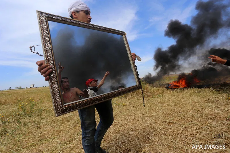 Palestinian protesters use a reflective mirror to divert the attention of members of the Israeli forces during a tent city protest at the Israel-Gaza border, in Khan Yunis in the southern Gaza Strip, on April 2, 2018. Ph...