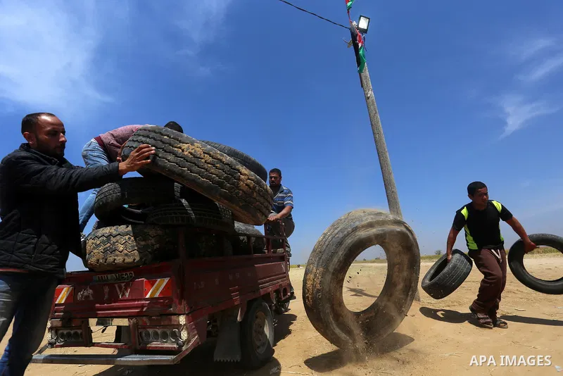 Palestinian protesters collect tires during a tent city protest at the Israel-Gaza border, in Khan Yunis in the southern Gaza Strip, on April 2, 2018. Photo by Yasser Qudih