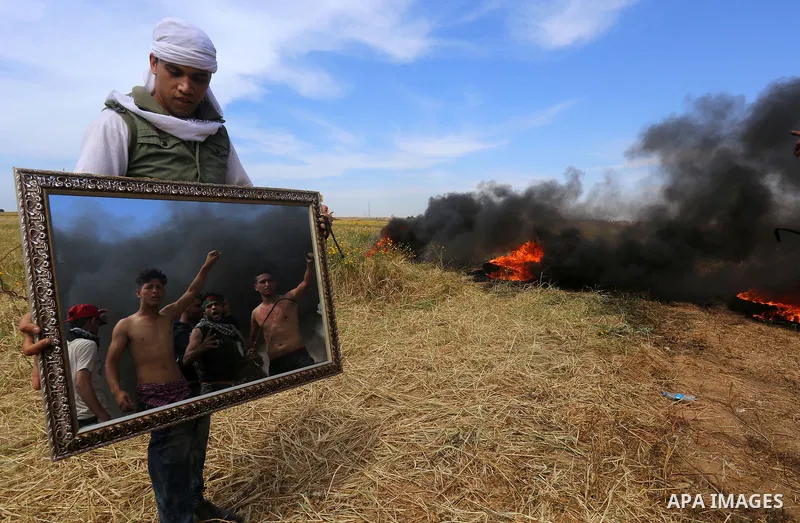 Palestinian protesters use a reflective mirror to divert the attention of members of the Israeli forces during a tent city protest at the Israel-Gaza border, in Khan Yunis in the southern Gaza Strip, on April 2, 2018. Ph...