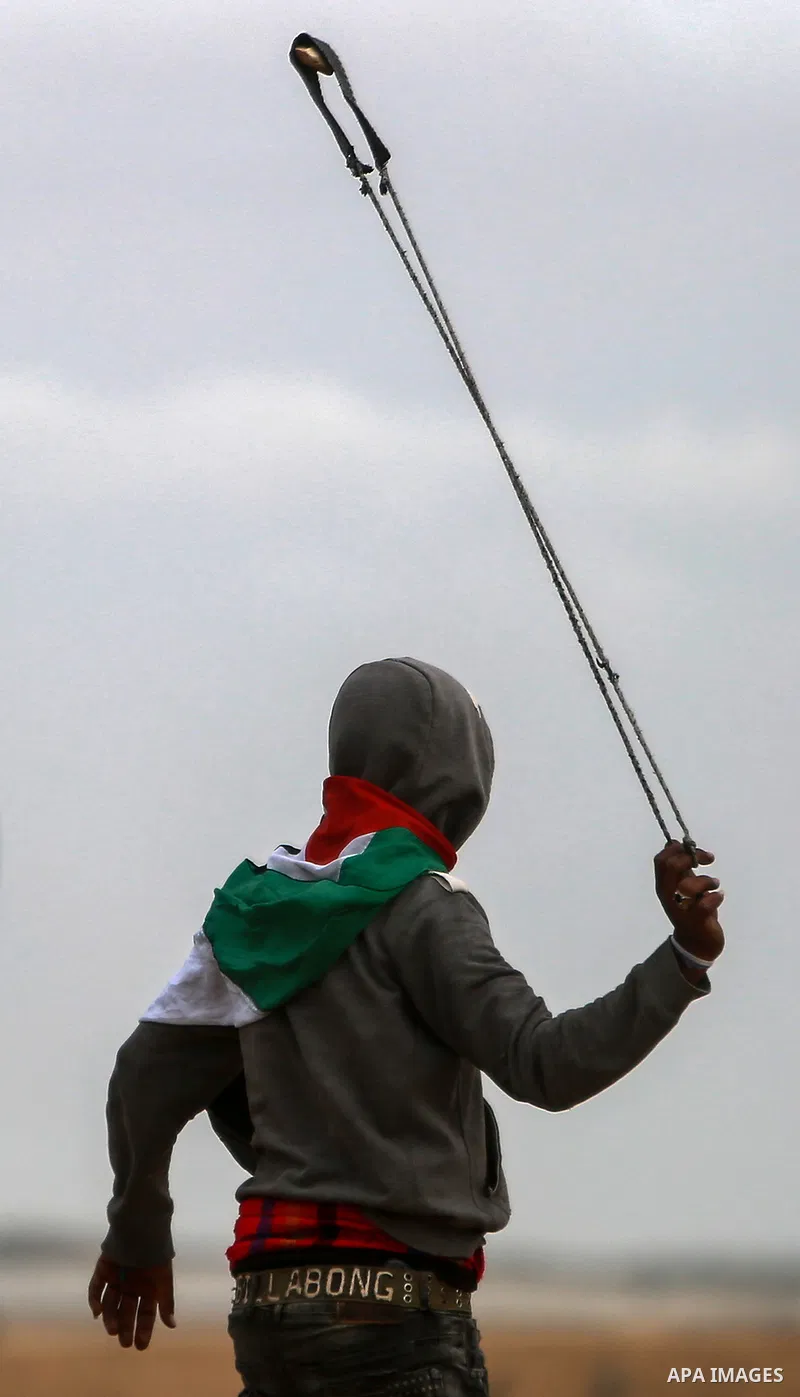 A Palestinian protester uses a slingshot to hurl stones towards Israeli security forces during clashes in a tent city protest along the Israel border with Gaza, demanding the right to return to their homeland, in the eas...