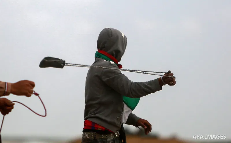 A Palestinian protester uses a slingshot to hurl stones towards Israeli security forces during clashes in a tent city protest along the Israel border with Gaza, demanding the right to return to their homeland, in the eas...
