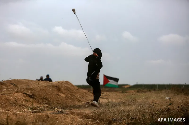 A Palestinian protester uses a slingshot to hurl stones towards Israeli security forces during clashes in a tent city protest along the Israel border with Gaza, demanding the right to return to their homeland, in the eas...