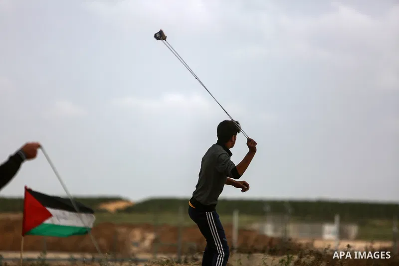 A Palestinian protester uses a slingshot to hurl stones towards Israeli security forces during clashes in a tent city protest along the Israel border with Gaza, demanding the right to return to their homeland, in the eas...