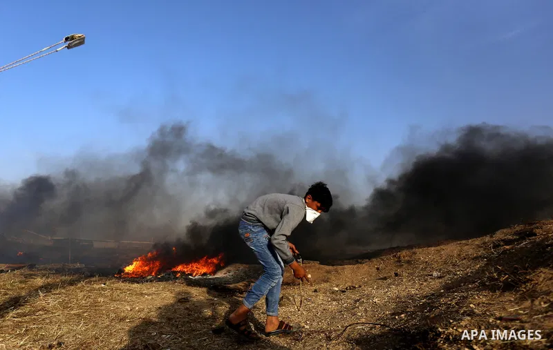 Palestinian protesters use a slingshot to hurl stones towards Israeli security forces during clashes in a tent city protest along the Israel border with Gaza, demanding the right to return to their homeland, in east of G...