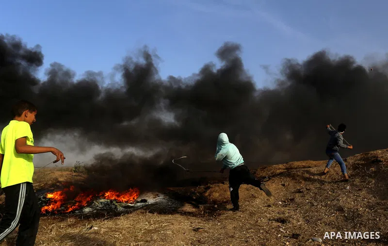 Palestinian protesters use a slingshot to hurl stones towards Israeli security forces during clashes in a tent city protest along the Israel border with Gaza, demanding the right to return to their homeland, in east of G...