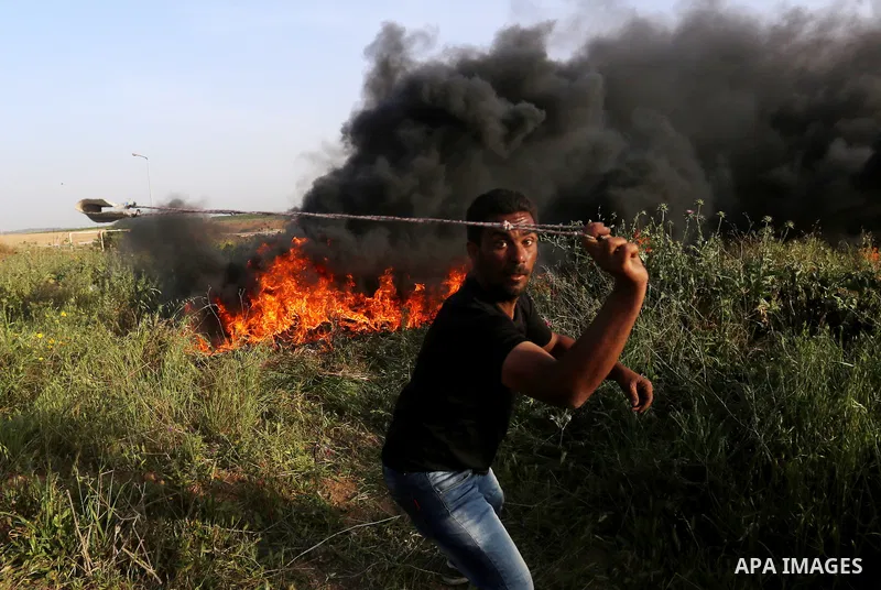 A Palestinian protester uses a slingshot to hurl stones towards Israeli security forces during clashes in a tent city protest along the Israel border with Gaza, demanding the right to return to their homeland, in east of...