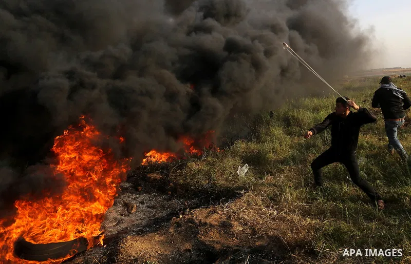 A Palestinian protester uses a slingshot to hurl stones towards Israeli security forces during clashes in a tent city protest along the Israel border with Gaza, demanding the right to return to their homeland, in east of...