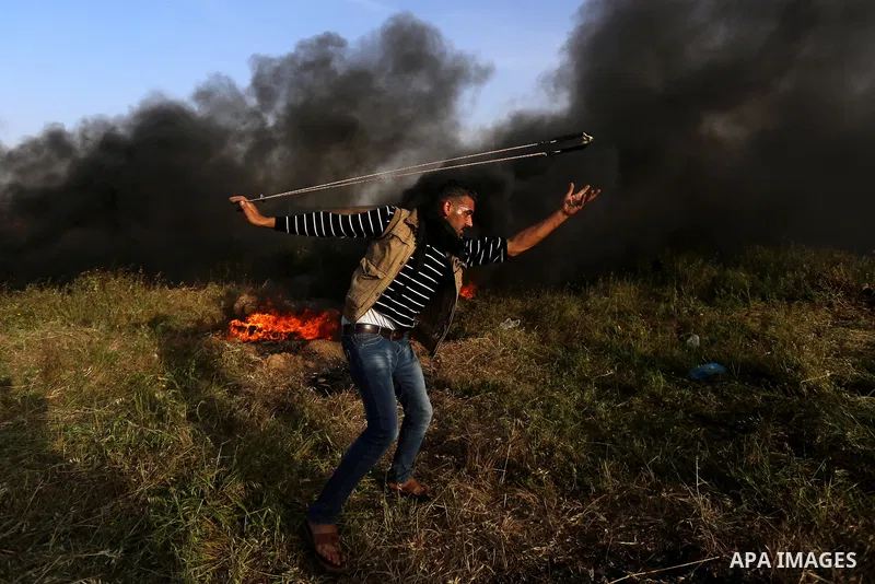 A Palestinian protester uses a slingshot to hurl stones towards Israeli security forces during clashes in a tent city protest along the Israel border with Gaza, demanding the right to return to their homeland, in east of...