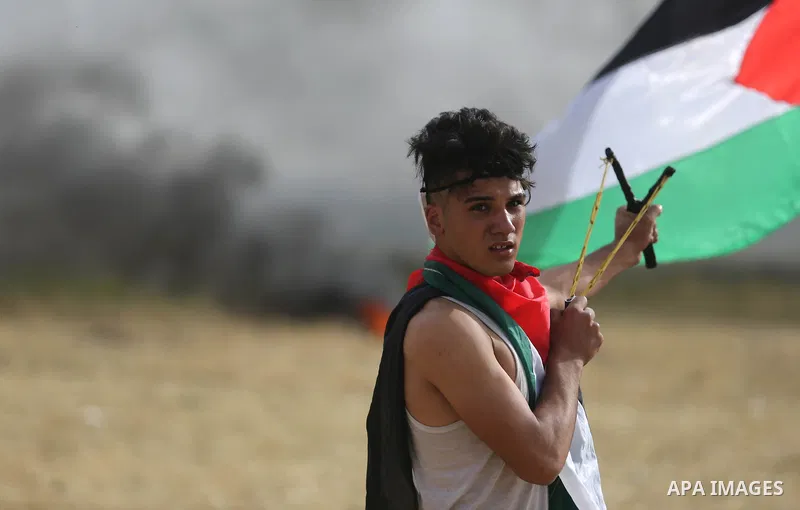 A Palestinian protester uses a slingshot to hurl stones towards Israeli security forces during clashes in a tent city protest at Israel-Gaza border, in the southern Gaza Strip April 5, 2018. Photo by Ashraf Amra