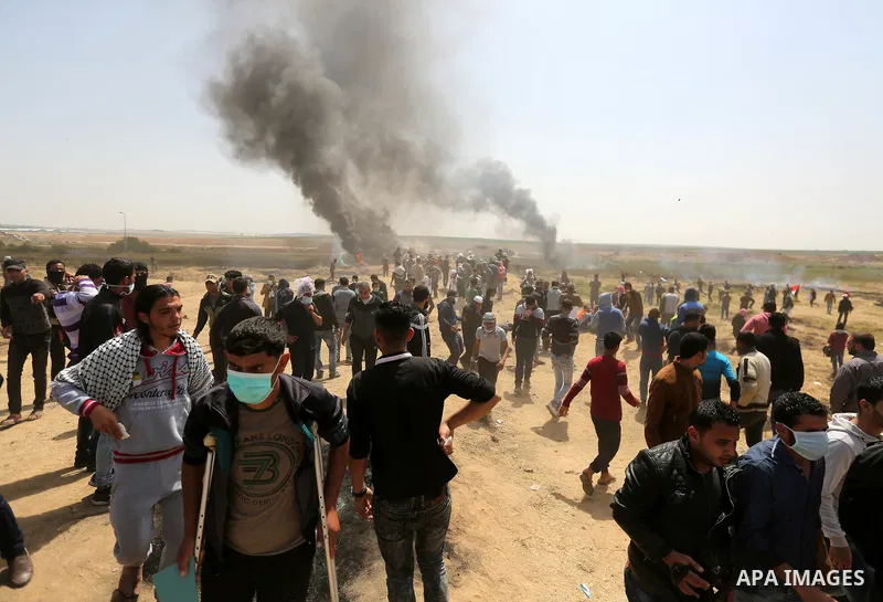 Palestinians run for cover from tear gas canisters fired by Israeli security forces during clashes at the Israel-Gaza border in a tent city protest demanding the right to return to their homeland, in east of Gaza city on...