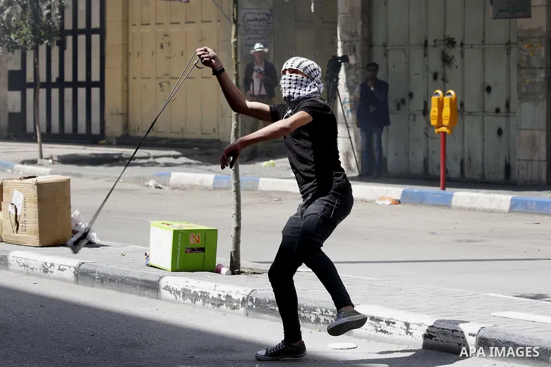 A Palestinian protester throws a stone towards Israeli soldiers during clashes following a demonstration, in the West Bank city of Hebron, on April 6, 2018. Photo by Wisam Hashlamoun
