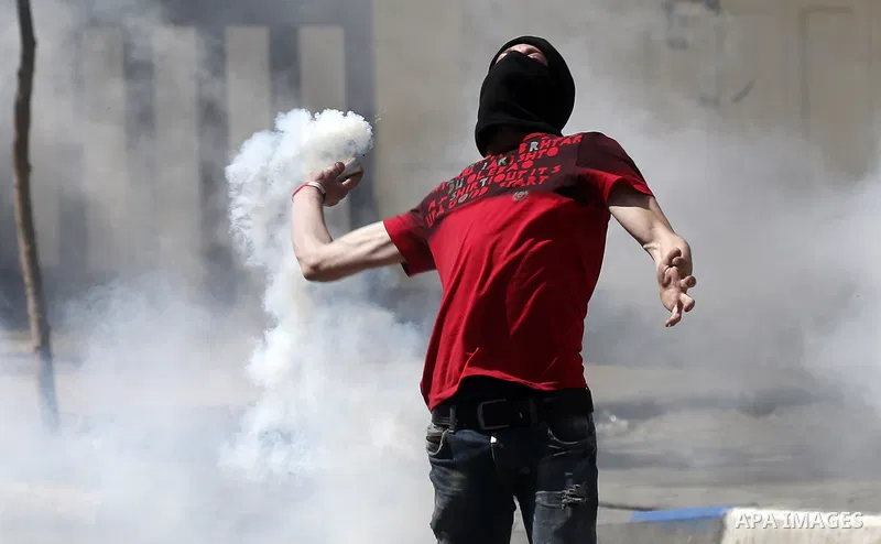 A Palestinian protester throws back a tear gas canister fired by Israeli security forces during clashes following a demonstration, in the West Bank city of Hebron, on April 6, 2018. Photo by Wisam Hashlamoun