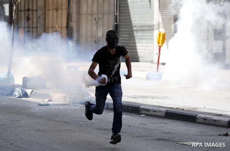 A Palestinian protester throws back a tear gas canister fired by Israeli security forces during clashes following a demonstration, in the West Bank city of Hebron, on April 6, 2018. Photo by Wisam Hashlamoun