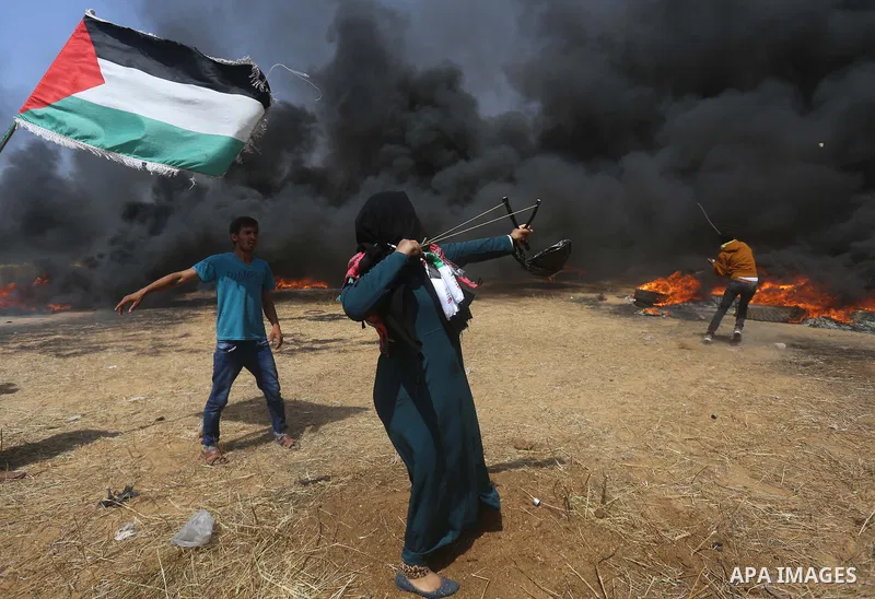 A Palestinian woman uses a slingshot to hurl stones towards Israeli security forces during clashes at the Israel-Gaza border in a tent city protest demanding the right to return to their homeland, in Khan Younis in the s...