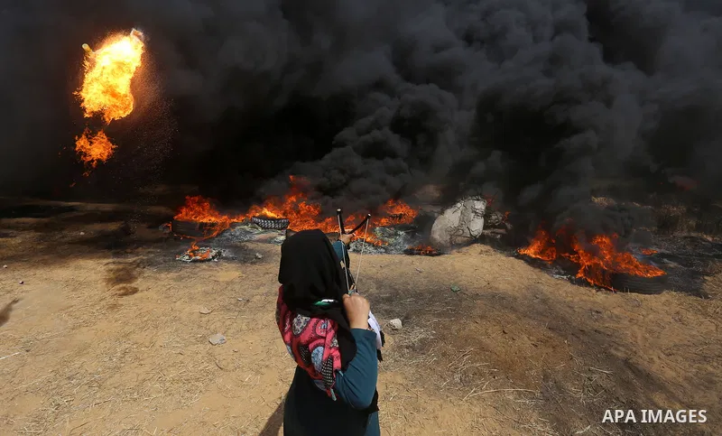 A Palestinian woman uses a slingshot to hurl stones towards Israeli security forces during clashes at the Israel-Gaza border in a tent city protest demanding the right to return to their homeland, in Khan Younis in the s...